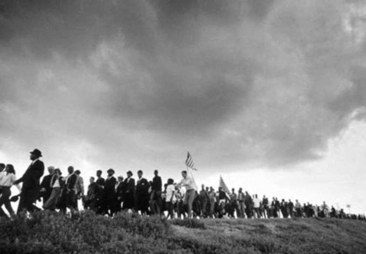 A long line of people marching for civil rights in Alabama under a large, ominous cloud 