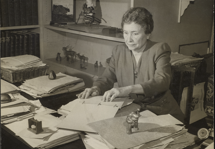 Photograph of Helen Keller seated at her desk and reading text in braille in Westport, Connecticut in 1950.