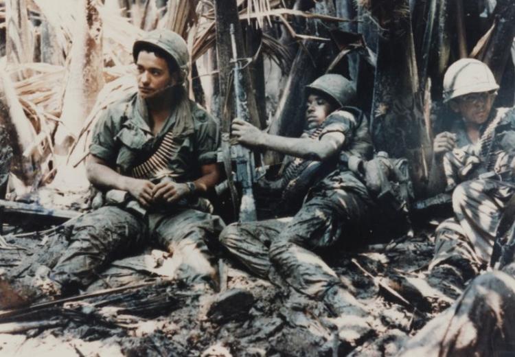 Privates First Class Carl Baden (New Orleans, Louisiana) and Arcadio Carrion (Puerto Rico) laying in the mud waiting for artillery to knock out the machine gun bunker that has them pinned down in a tree line at My Tho (April 4, 1968).