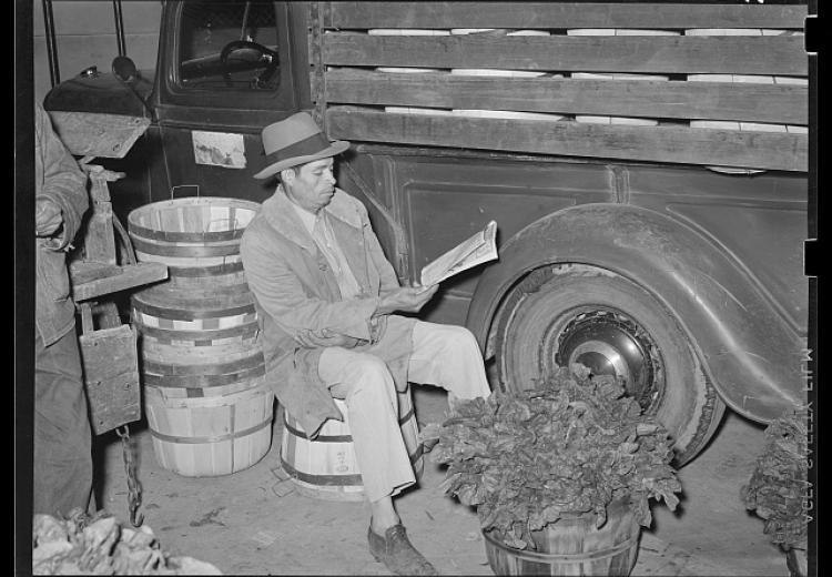 Mexican spinach peddler reading the newspaper about 4:30 in the morning. San Antonio, Texas
